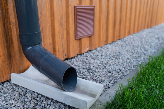 Close-up of a plastic gutter on the corner of a building made of metal siding and a cement drainage channel. Foundation ventilation and vents, waterproofing for a private home