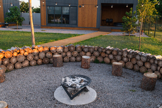 Outdoor gathering area featuring circular stone wall, log seating and central firepit surrounded by evening lights