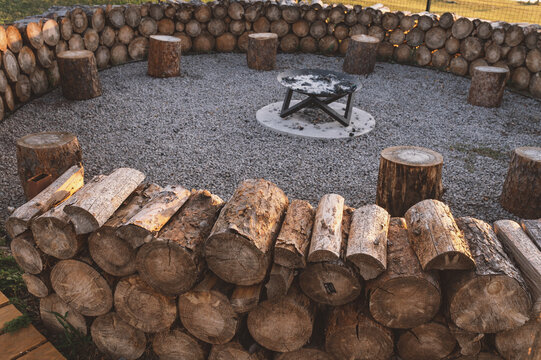 Natural stone firepit with wooden log benches arranged around central metal fire bowl in backyard