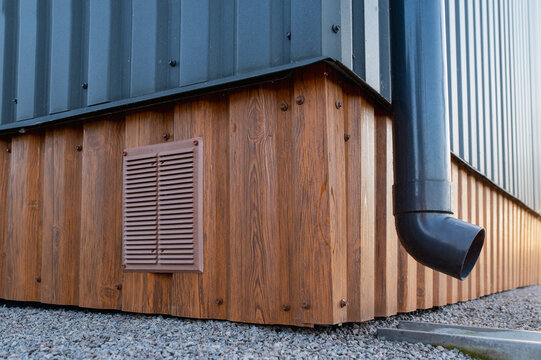 Close-up of a plastic gutter on the corner of a building made of metal siding and a cement drainage channel and Ventilation grille
