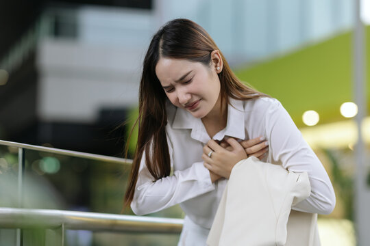 asian woman holding chest experiencing sudden severe pain heart attack showing distressed expression agony from health illness