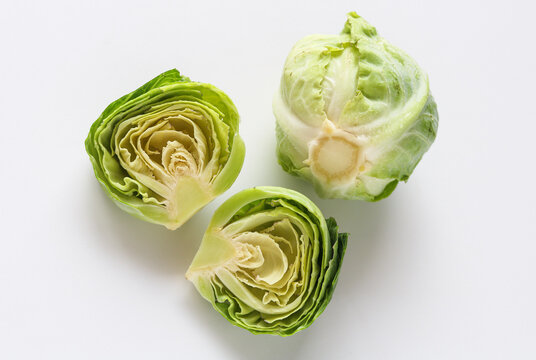 A view of three fresh, baby cabbages, two halves and one whole, arranged on a clean white background.