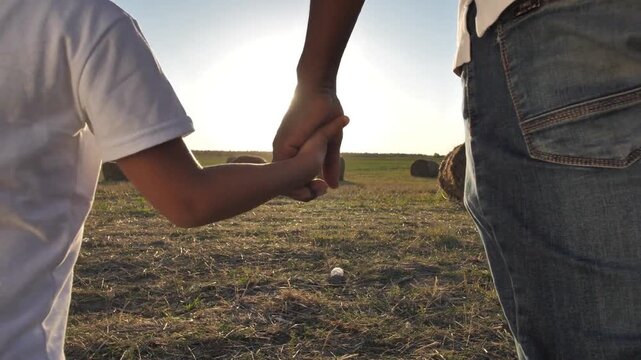 Close up family male man father parent dad holding hands little boy child son kid arm bonding closeness support happy childhood teamwork fatherhood outside rural meadow field. farmer farm countryside