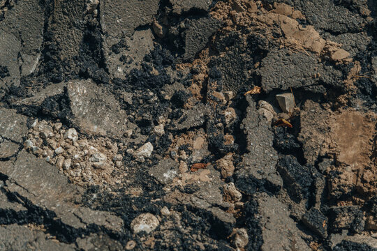 Macro shot of destroyed asphalt pavement with cracks and gravel during road reconstruction works.