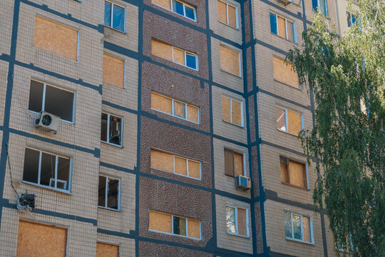 Residential multi-story apartment building with windows boarded up with plywood and OSB sheets after explosion damage.
