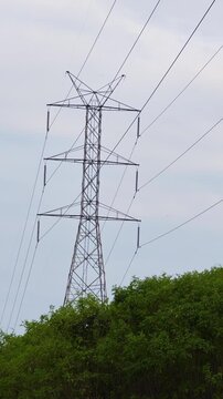 : High voltage electricity transmission towers standing on a mountain ridge, surrounded by a natural landscape under daylight.