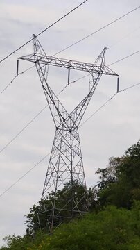 : High voltage electricity transmission towers standing on a mountain ridge, surrounded by a natural landscape under daylight.