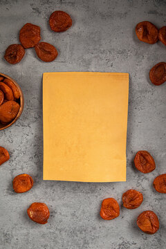 Blank kraft paper zipper pouch packaging mockup surrounded by dried apricots on dark stone table top view