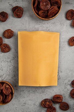 Natural dark dried apricots in wooden bowls and scattered around craft paper ziplock pouch mockup top view