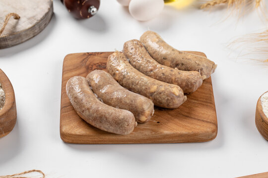 Raw meat kupat sausages arranged on wooden cutting board on white tabletop with ingredients around