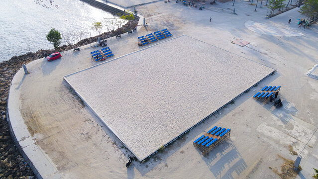 Aerial view of a rectangular sand court surrounded by blue spectator seating near the coastline in Indonesia.