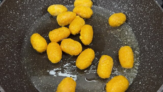 In a cozy home kitchen, 14 small hot dogs are frying in hot oil on a large cast-iron skillet, sizzling and turning golden brown, a quick and tasty comfort meal, a candid authentic life moment.