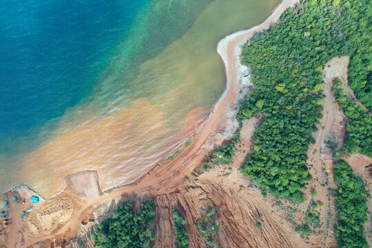 Aerial view of the PT Ceria Nugraha Indotama mining site showing sediment runoff flowing into the blue sea near the forested coastline in Wolo, South East Sulawesi, Indonesia.