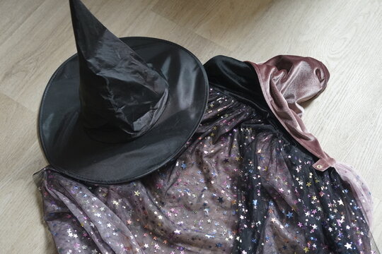 Black witch hat and iridescent sequin star fabric resting on wooden floor with dramatic Halloween silhouette and festive sparkle closeup for costume styling still life