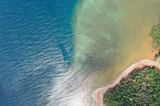 Aerial view of PT Ceria Nugraha Indotama mining site, showing contrast between blue sea, turquoise water, and red earth near lush vegetation in Wolo, South East Sulawesi, Indonesia.