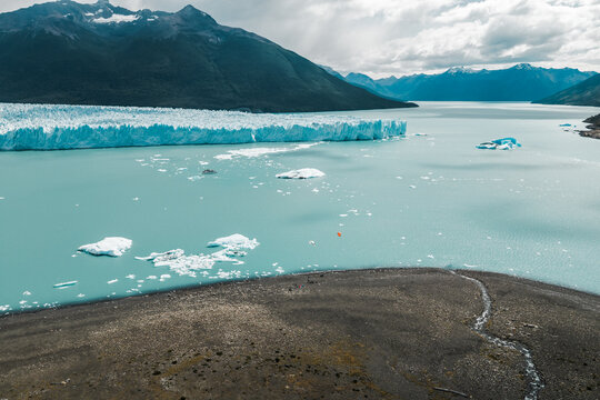 Aerial view of Perito Moreno Glacier with turquoise glacial water, floating icebergs, and rocky shoreline in the background of mountains in Perito Moreno, Santa Cruz Province, Argentina.
