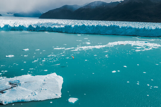Aerial view of Perito Moreno Glacier with a kite surfer gliding over turquoise water filled with floating icebergs in Perito Moreno, Santa Cruz Province, Argentina.