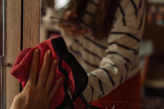 Hand wiping a mirror with a red cloth beside a woman's reflection.
