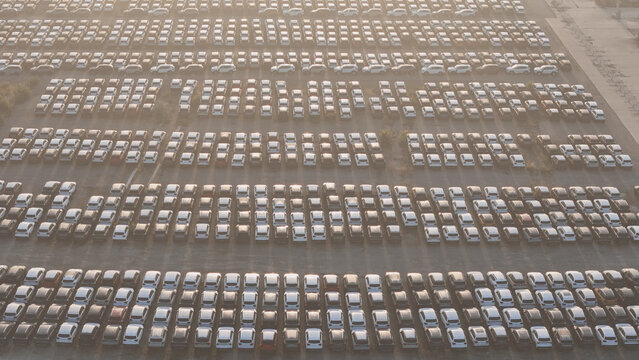 Large automobile distribution center showing hundreds of new cars and SUVs parked in rows, awaiting shipment for import and export global commerce and trading logistics