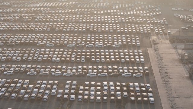 New cars and suvs filling a vast outdoor lot, organized in perfect rows, reflecting automotive manufacturing, global trade, distribution, and logistics operations