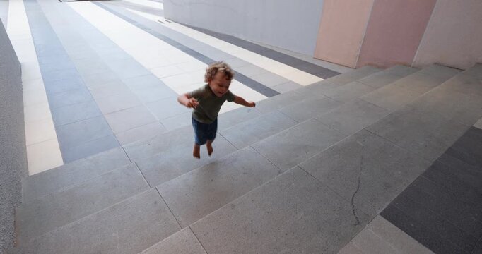 Toddler jumping up wide shallow stairs, pausing to coordinate movements and balance before turning around to jump down. Scene of active childhood play and gross motor skills development
