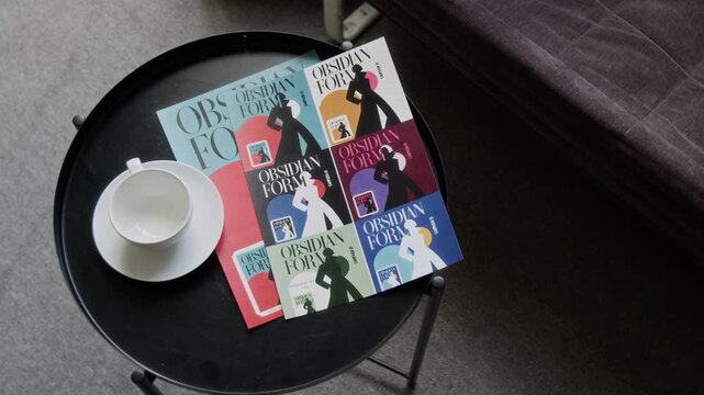Graphic design magazines lying beside empty ceramic cup on small table, high angle view. Clip suitable for publishing house advertising, book marketing, editorial projects