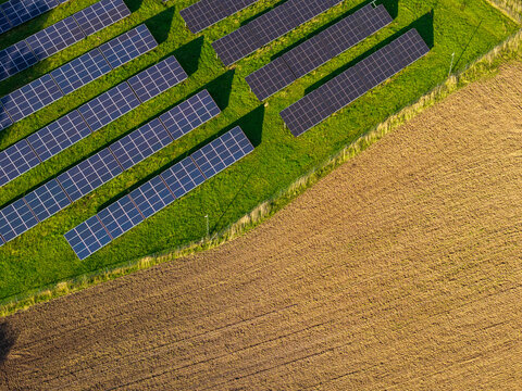 Aerial view of solar panels arranged in rows on a green field adjacent to a large cultivated agricultural plot in Ziezmariai, Kaunas County, Lithuania.