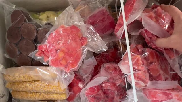 Person's viewpoint exploring a chest freezer full of frozen vegetables, cold air, frosty bags, labels, ice crystals, candid authentic life moment in a home kitchen today