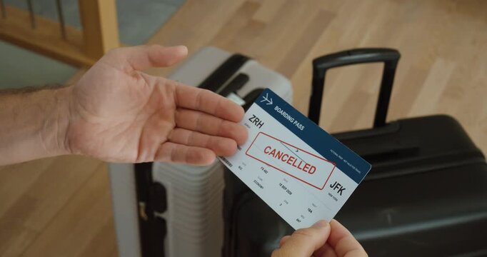 Traveler holding a cancelled boarding pass from Zurich to New York in front of luggage, representing flight cancellation and disrupted travel. close up