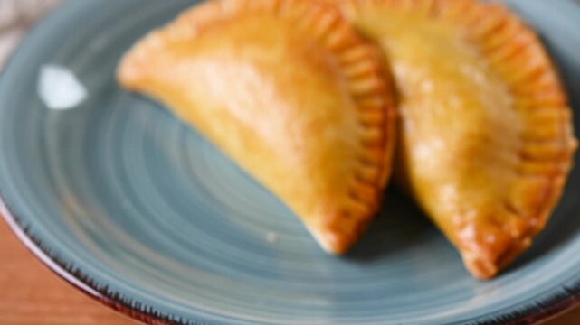 Close-up of a hand picking up a homemade empanada from a plate, showing a traditional savory pastry ready to eat.