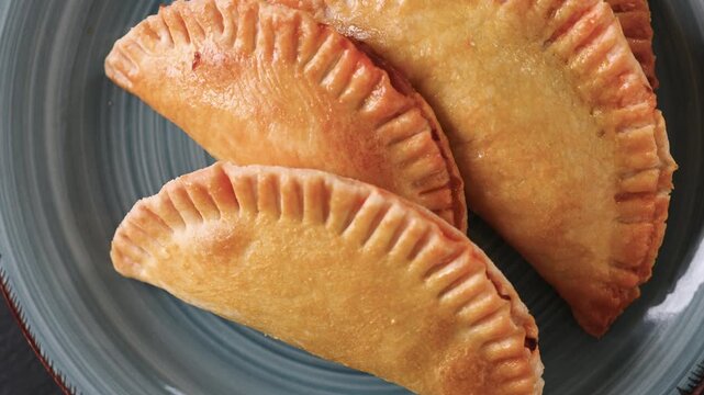 Plate of golden homemade empanadas rotating slowly, showcasing traditional savory pastries ready to serve and eat.