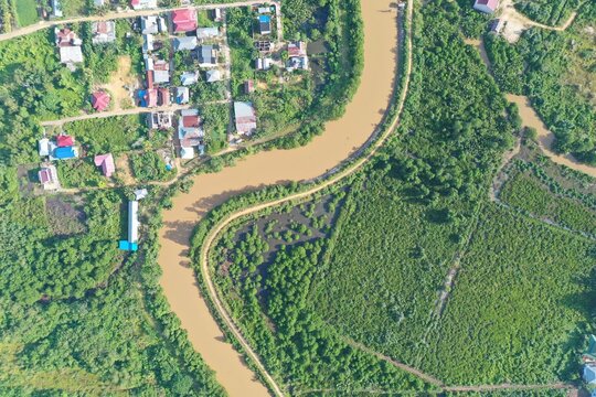 Aerial view of a winding river flowing through a lush green landscape with residential houses and dense vegetation in Kendari, South East Sulawesi, Indonesia.