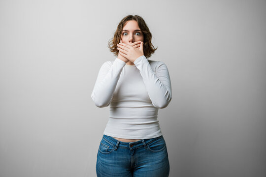 Woman casual covering mouth with hands, cover hand pressed to lips in shock after a mistake, secret revealed, shocked expression against white background