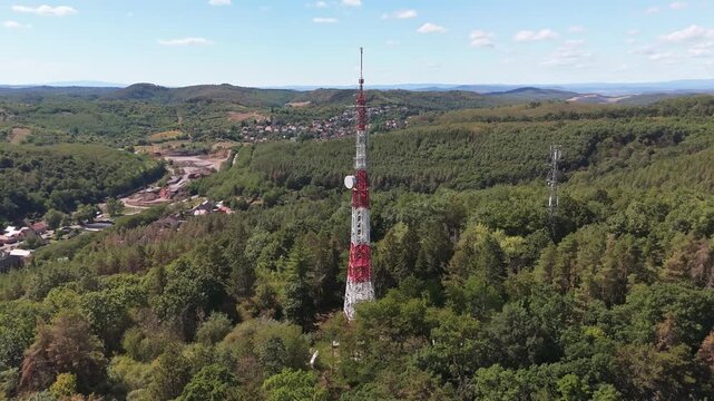 Salg&oacute;tarj&aacute;n, Hungary radio and TV transmission tower on forested hills in summer, with telecom infrastructure and network relay equipment, panoramic landscape captured by drone.