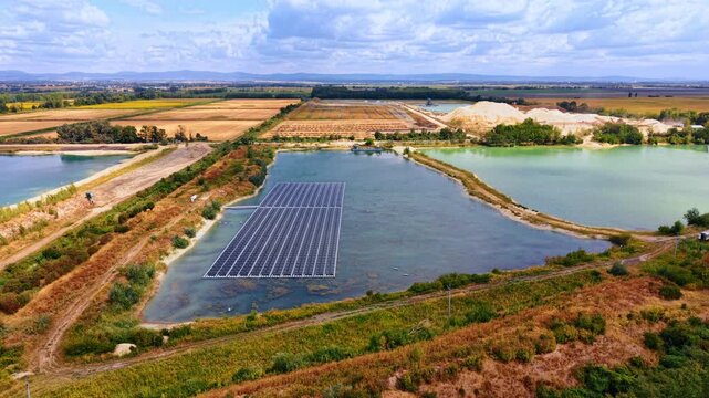 Water based solar power station near agriculture.. An artificial reservoir contains a rectangular photovoltaic array bordered by overgrown banks and distant farming fields.