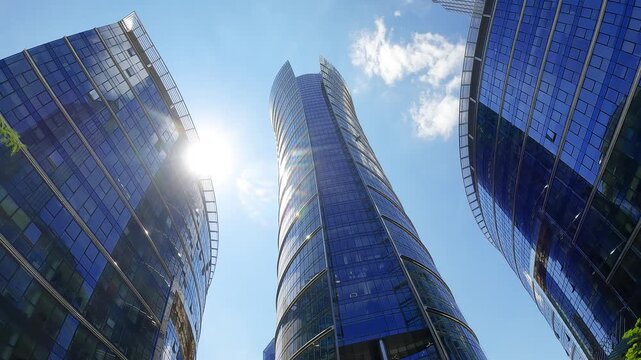 Modern corporate skyscrapers with blue glass facades rising towards the bright sky. Urban business district architecture with green trees