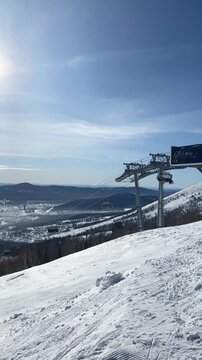 A snowy ski slope with cables and chairs under a clear blue sky, showcasing the winter sports area in the mountainous landscape of Mount Mustag in Sheregesh