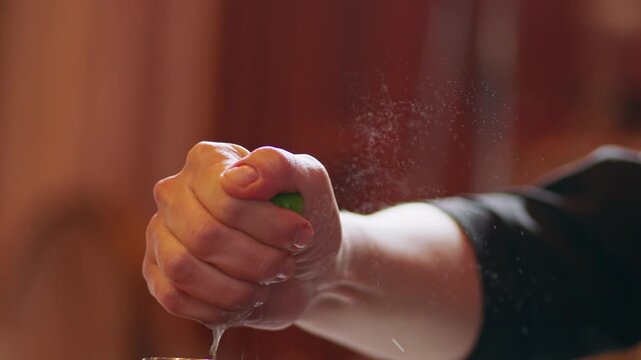 Extreme close up shot of a chef or bartender's hand firmly squeezing a fresh green lime, extracting bright juice droplets for a culinary recipe or craft cocktail