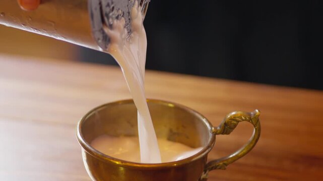 Close up shot of a professional bartender pouring a smooth, white Ayran yogurt drink from a shaker into an elegant glass, highlighting the creamy and frothy texture of this savory beverage