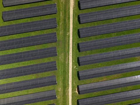 Aerial view of solar panels arranged in parallel rows separated by a dirt path in The Basin, Victoria, Australia.