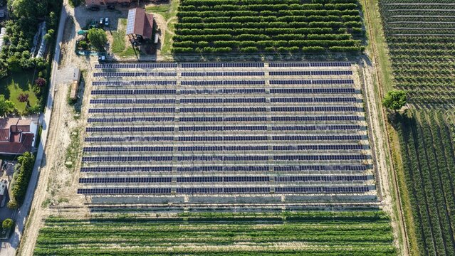 Aerial view of a large solar panel farm situated in the rural landscape of Faenza, surrounded by agricultural fields and orchards in Faenza, Emilia-Romagna, Italy.