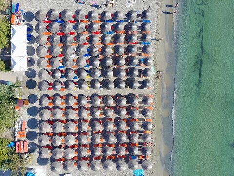 Aerial view of rows of straw umbrellas and sun loungers on the sandy beach of Katarinies Paralia, Greece.