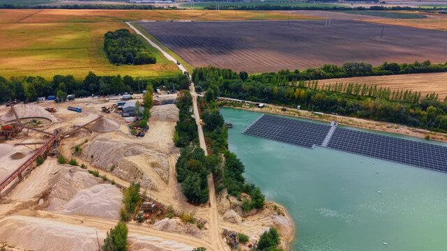 Sand mining facility next to solar lake. Aerial viewpoint captures a sand processing plant adjacent to a water body with floating solar panels.
