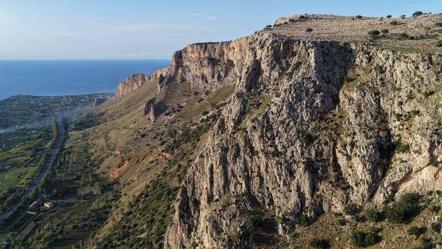 Aerial view of the rugged coastal cliffs of Terrasini, featuring steep rocky slopes, sparse vegetation, and a view of the Mediterranean Sea along the coastline in Terrasini, Sicily, Italy.