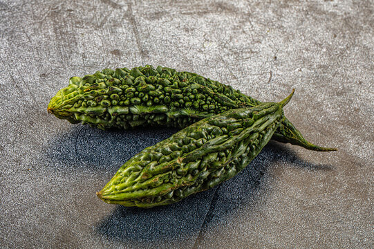 Two fresh green bitter gourds with textured skin on gray stone surface, natural lighting and soft shadows