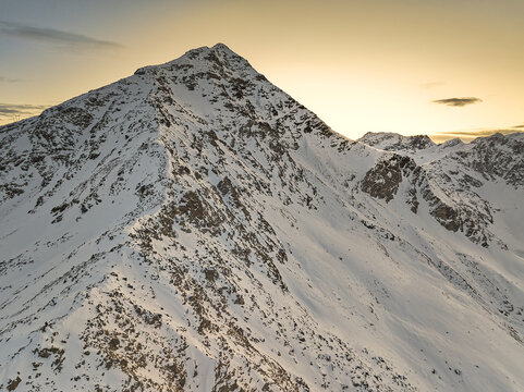 Aerial view of Valchiavenna mountain peak covered in snow during golden hour in Lombardy, Italy.
