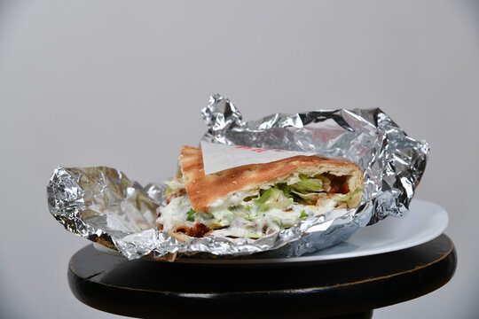 Ge&ouml;ffneter D&ouml;ner Kebab mit Fleisch, Salat, Gem&uuml;se und cremiger Sauce in Aluminiumfolie auf einem Teller. Street Food, Imbiss, Take-away, Fast Food und authentische Food-Fotografie.