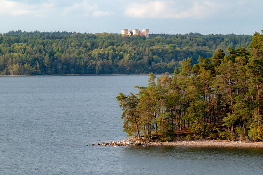 A scenic view of a majestic historic castle nestled among lush green forests along a tranquil Scandinavian waterway near Stockholm, Sweden.