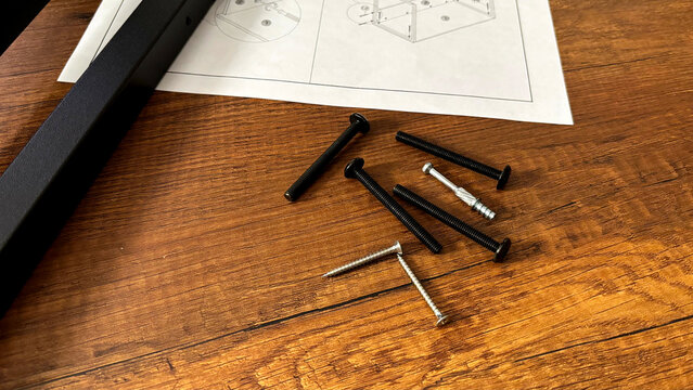 Furniture assembly hardware screws bolts and instruction manual sheet on wooden table