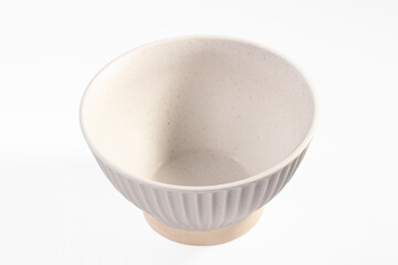 Empty ceramic bowl with fluted sides and speckled beige glaze on white background